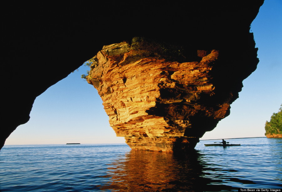 Kayaker passing cave, Lake Superior, Wisconsin, USA